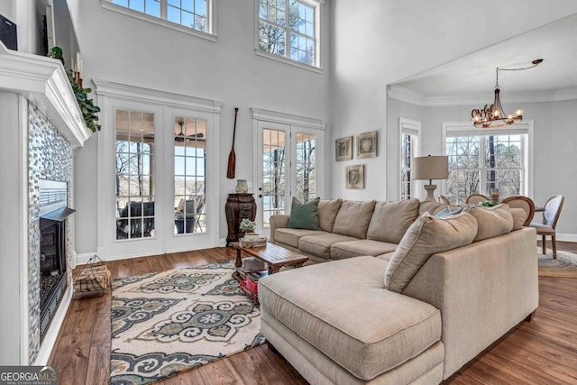 living room featuring wood-type flooring, crown molding, a notable chandelier, a premium fireplace, and french doors