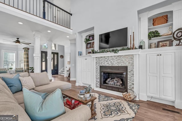 living room with light hardwood / wood-style flooring, built in features, a tile fireplace, ceiling fan, and decorative columns