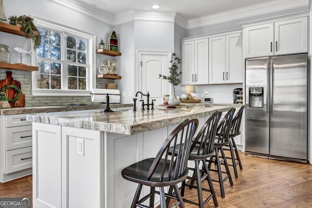 kitchen with white cabinetry, stainless steel fridge, and a center island with sink