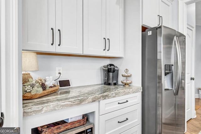 interior space featuring white cabinetry, stainless steel refrigerator with ice dispenser, and light stone counters