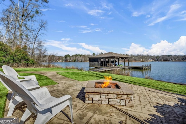 view of dock featuring a water view, an outdoor fire pit, a patio area, and a lawn