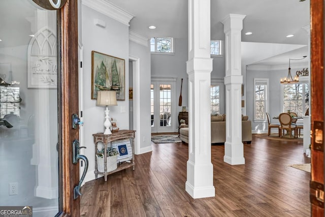 entryway featuring ornate columns, ornamental molding, dark wood-type flooring, and a notable chandelier