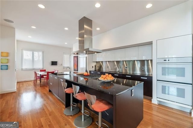 kitchen featuring island range hood, a kitchen breakfast bar, stainless steel gas stovetop, and a large island with sink