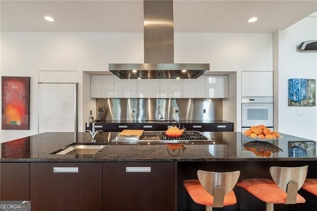 kitchen with island range hood, dark stone counters, stainless steel gas stovetop, and white oven