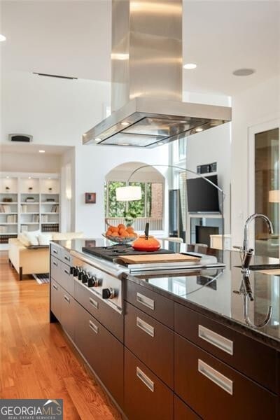 kitchen featuring sink, island range hood, dark brown cabinets, hardwood / wood-style flooring, and stainless steel gas stovetop