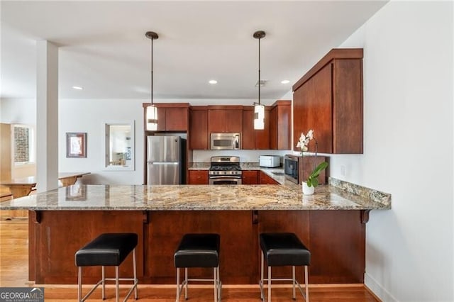 kitchen featuring pendant lighting, appliances with stainless steel finishes, light stone countertops, a kitchen bar, and kitchen peninsula