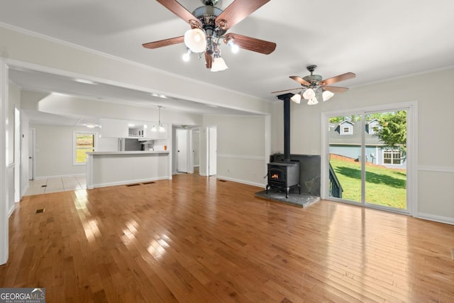 unfurnished living room featuring crown molding, a wood stove, ceiling fan, and light wood-type flooring