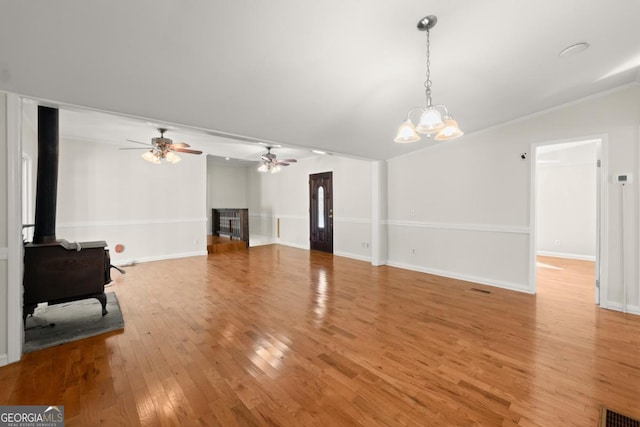 living room featuring ornamental molding, a wood stove, ceiling fan with notable chandelier, and light hardwood / wood-style floors