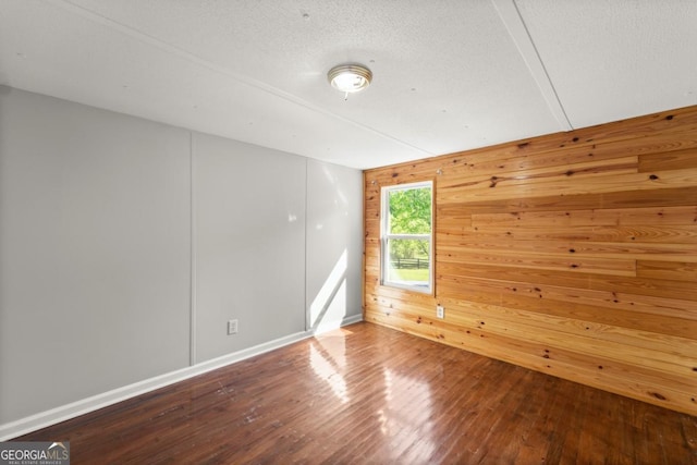 spare room with wood-type flooring, wooden walls, and a textured ceiling