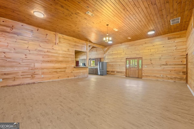 unfurnished living room with wooden walls, a chandelier, wood ceiling, and light hardwood / wood-style floors