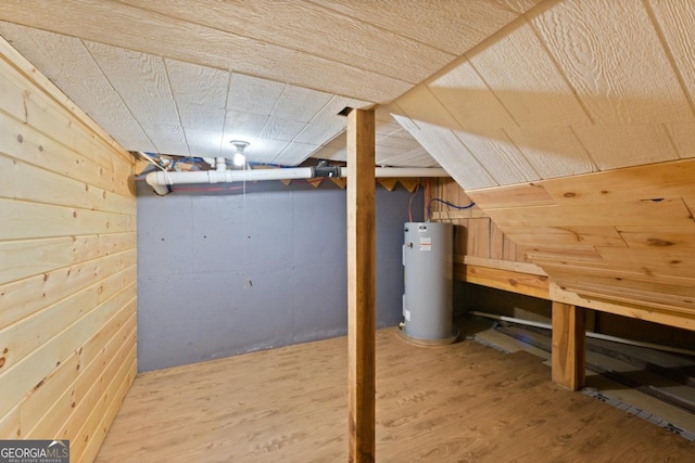 basement featuring hardwood / wood-style floors, wooden walls, and water heater