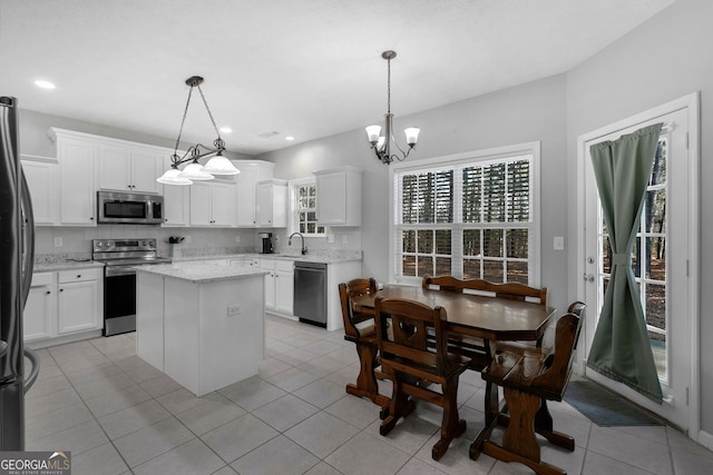 kitchen with appliances with stainless steel finishes, a center island, decorative light fixtures, and a sink