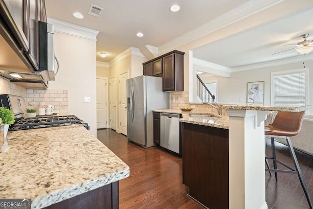 kitchen with appliances with stainless steel finishes, dark hardwood / wood-style floors, a breakfast bar area, light stone countertops, and dark brown cabinets