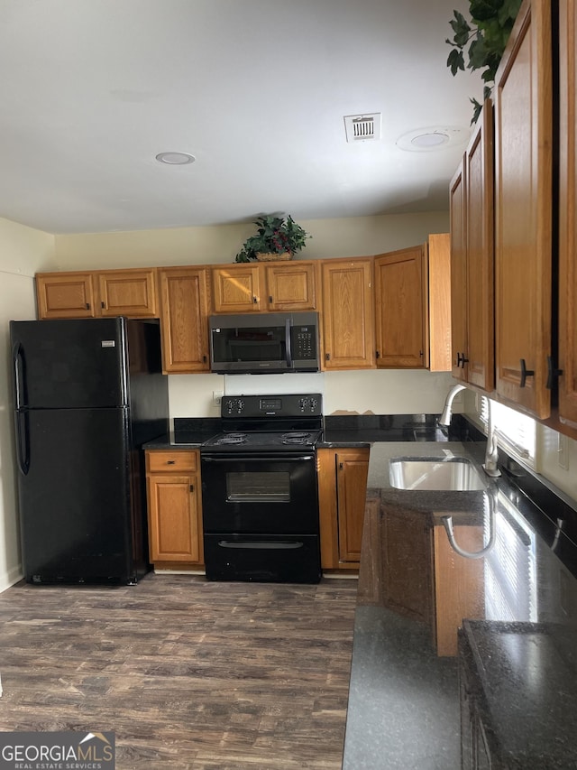 kitchen featuring visible vents, dark wood-type flooring, black appliances, a sink, and brown cabinetry