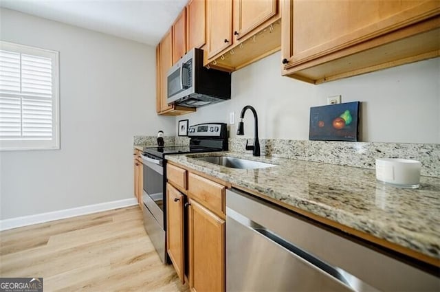 kitchen featuring light stone counters, appliances with stainless steel finishes, light hardwood / wood-style floors, and sink