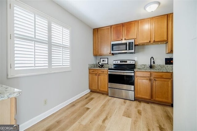 kitchen with stainless steel appliances, sink, light stone counters, and light hardwood / wood-style floors