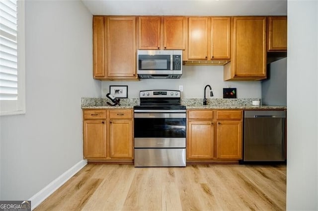 kitchen featuring stainless steel appliances, sink, light stone counters, and light hardwood / wood-style floors