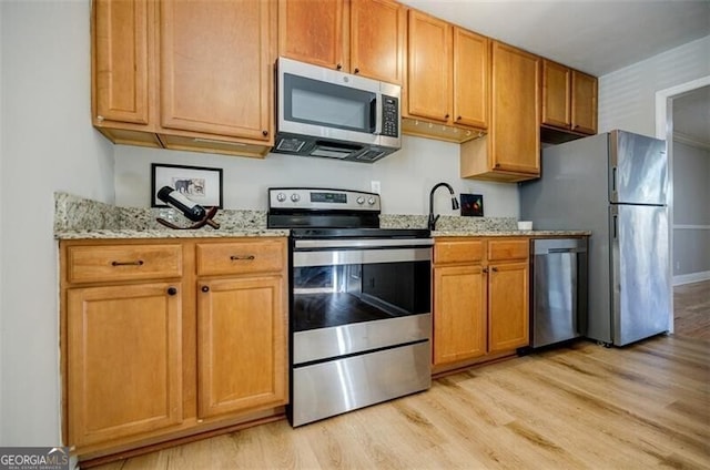 kitchen featuring light stone counters, light wood-type flooring, and appliances with stainless steel finishes