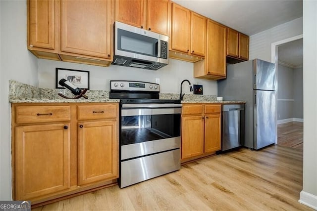 kitchen featuring appliances with stainless steel finishes, light stone counters, and light hardwood / wood-style floors