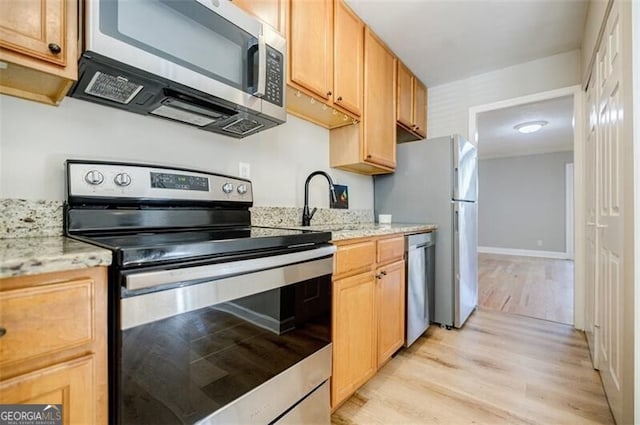 kitchen with stainless steel appliances, light stone countertops, sink, and light hardwood / wood-style flooring