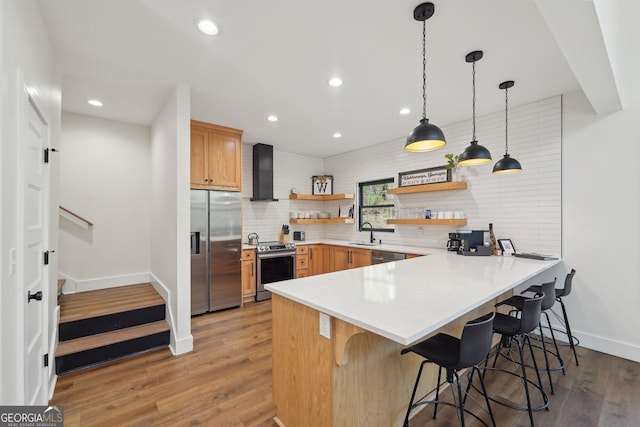 kitchen featuring a breakfast bar, hanging light fixtures, appliances with stainless steel finishes, kitchen peninsula, and wall chimney range hood