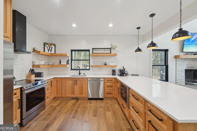 kitchen with wall chimney exhaust hood, sink, kitchen peninsula, pendant lighting, and stainless steel appliances