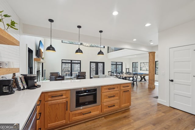 kitchen featuring decorative columns, hanging light fixtures, stainless steel dishwasher, light hardwood / wood-style floors, and kitchen peninsula