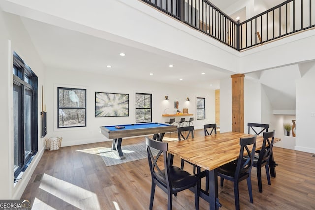 dining area featuring decorative columns, wood-type flooring, a towering ceiling, and pool table