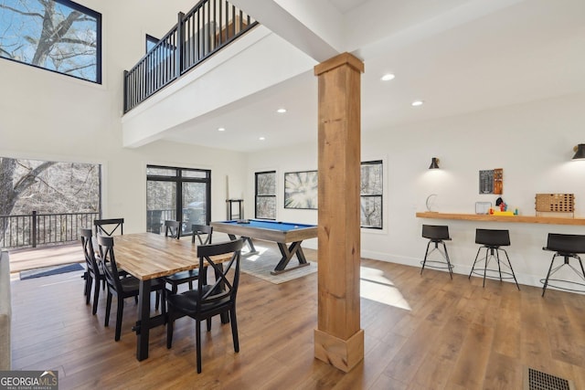 dining area with hardwood / wood-style flooring, a towering ceiling, pool table, and decorative columns