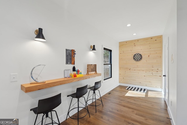 kitchen with hardwood / wood-style floors, a breakfast bar area, kitchen peninsula, and wood walls