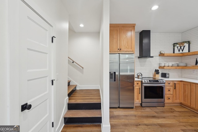 kitchen with decorative backsplash, light hardwood / wood-style flooring, wall chimney exhaust hood, and appliances with stainless steel finishes