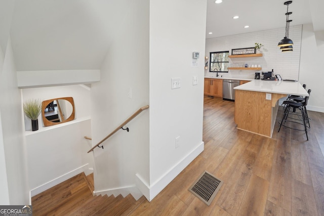 kitchen featuring a breakfast bar, hanging light fixtures, stainless steel dishwasher, kitchen peninsula, and light wood-type flooring