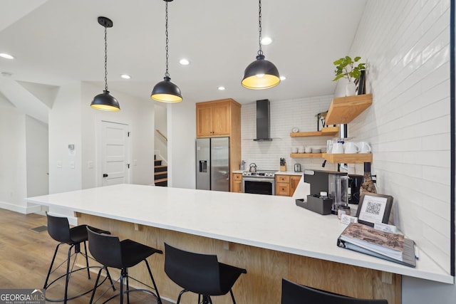 kitchen with a breakfast bar area, hanging light fixtures, stainless steel appliances, wood-type flooring, and wall chimney exhaust hood