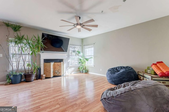 living room with a ceiling fan, a fireplace, baseboards, and wood finished floors