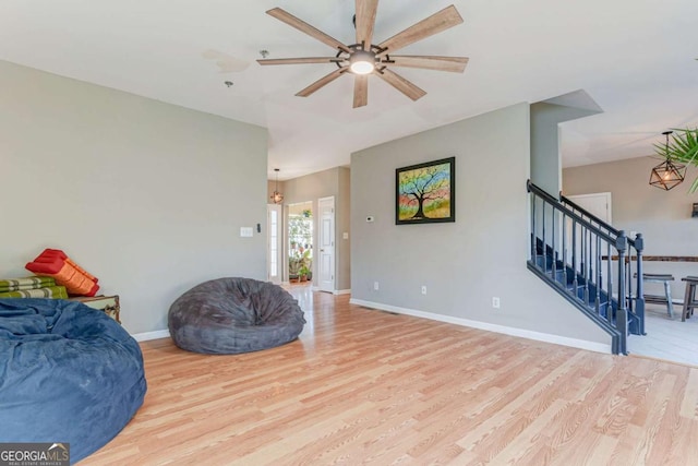 sitting room featuring stairs, light wood-type flooring, a ceiling fan, and baseboards