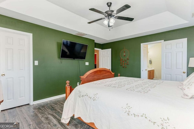 bedroom with ensuite bathroom, wood finished floors, a ceiling fan, baseboards, and a raised ceiling