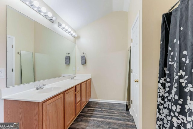 bathroom with double vanity, vaulted ceiling, a sink, wood finished floors, and baseboards