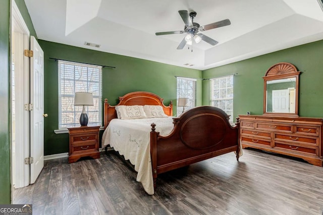 bedroom with multiple windows, dark hardwood / wood-style flooring, a raised ceiling, and ceiling fan