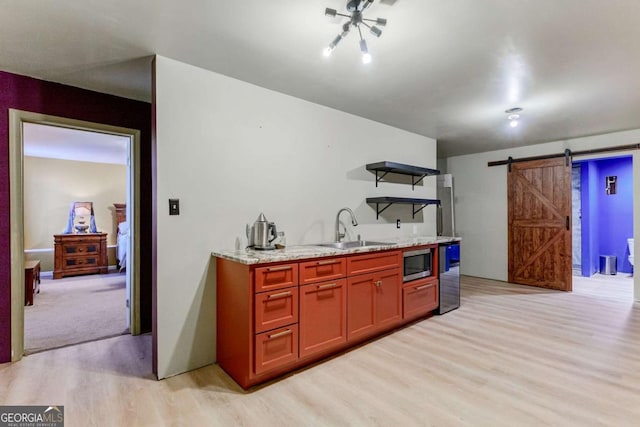 kitchen with open shelves, stainless steel microwave, a barn door, a sink, and light wood-type flooring