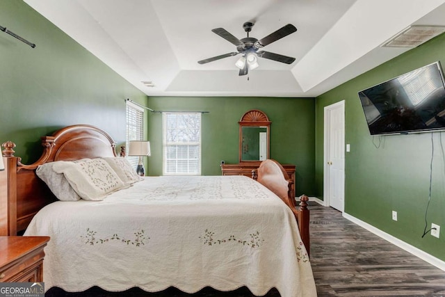 bedroom with ceiling fan, dark hardwood / wood-style floors, and a raised ceiling