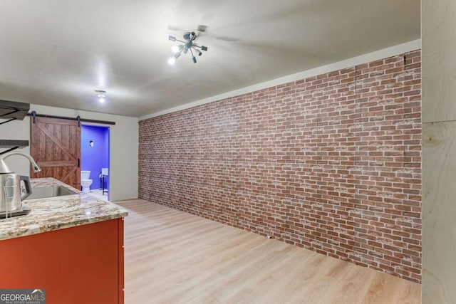 kitchen featuring brick wall, sink, a barn door, light stone countertops, and light wood-type flooring