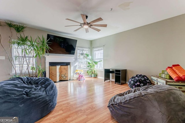 living area featuring light wood finished floors, a fireplace, a ceiling fan, and baseboards