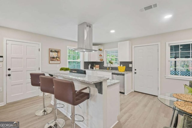 kitchen featuring dishwasher, island exhaust hood, white cabinets, a kitchen island, and decorative backsplash