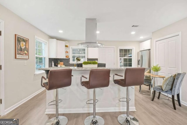 kitchen featuring light stone counters, island exhaust hood, a breakfast bar area, and white cabinets