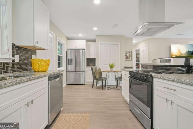 kitchen with light hardwood / wood-style flooring, appliances with stainless steel finishes, light stone counters, island range hood, and white cabinets