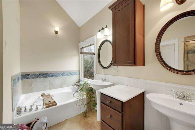 bathroom with a tub to relax in, vaulted ceiling, and dual sinks