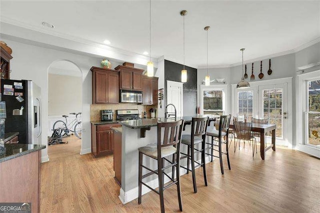 kitchen featuring light hardwood / wood-style flooring, appliances with stainless steel finishes, ornamental molding, a center island with sink, and decorative light fixtures