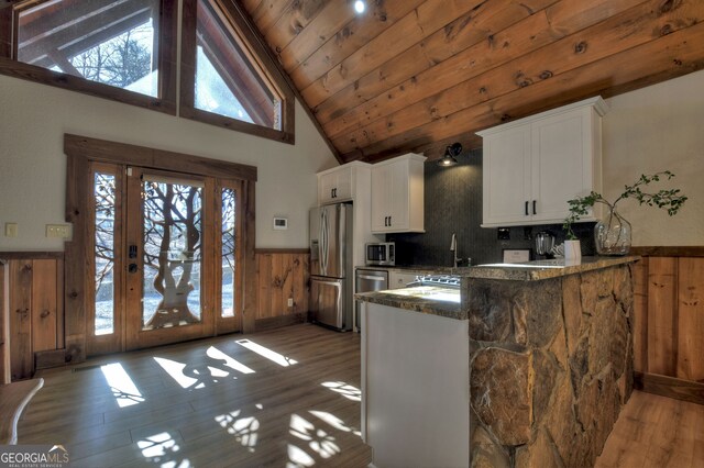 kitchen featuring wood walls, white cabinetry, dark stone countertops, appliances with stainless steel finishes, and kitchen peninsula