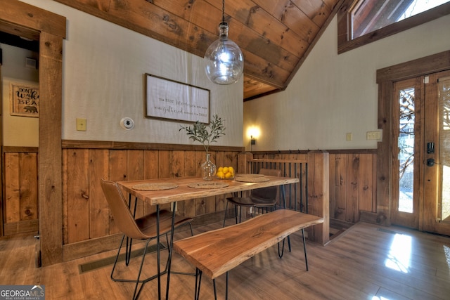 dining space with light hardwood / wood-style flooring, wooden ceiling, wood walls, and vaulted ceiling