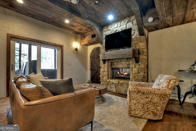 living room featuring hardwood / wood-style floors, a stone fireplace, and beamed ceiling